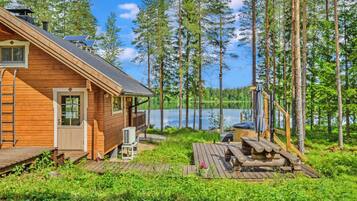 Une cabane en bois dotée d’une terrasse, d’un bain à remous et offrant une vue sur un lac entouré d’arbres.