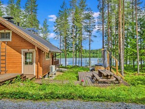 A wooden cabin with a deck, a hot tub, and a view of a lake surrounded by trees.