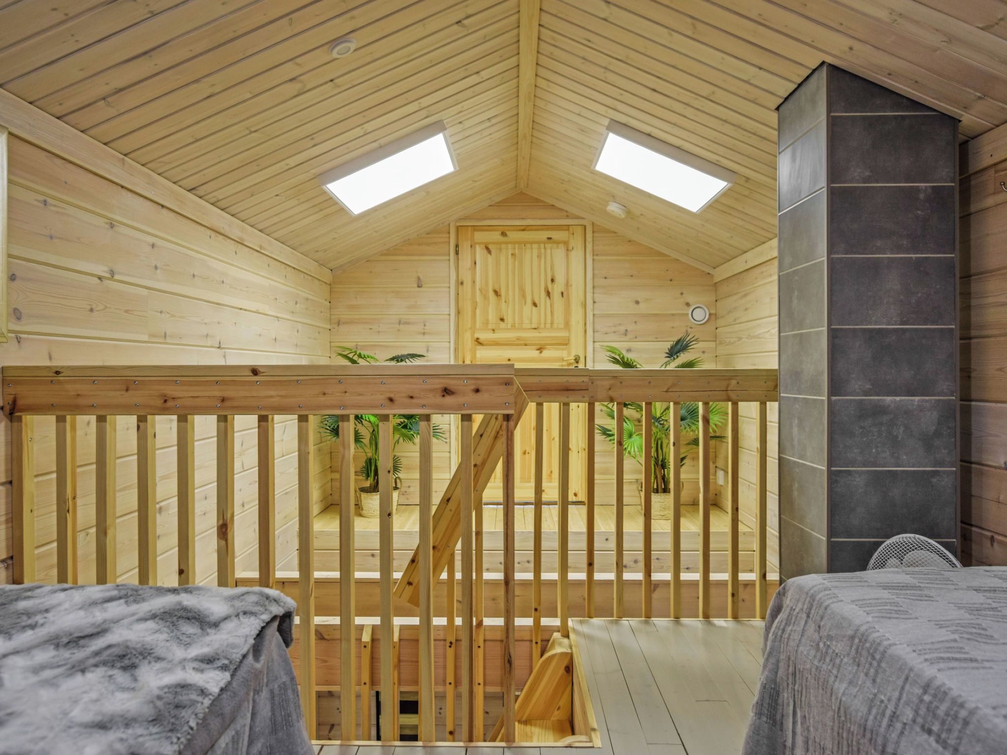 Ein Holzinnenraum mit hoher Decke, zwei Oberlichtern, einer Holztür und einem Steinkamin.