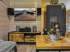 A cozy living room with a flat-screen TV mounted on the wall, a fireplace, wooden furniture, and a potted plant.