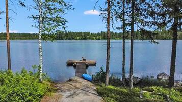 Järvi, jonka rannalla on laituri, joka ulottuu veden päälle. Järveä ympäröivät puut ja taivaalla on kirkas, selkeä sää.