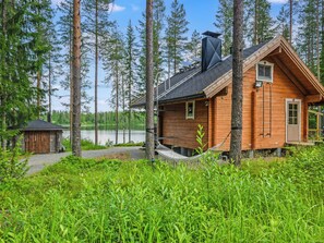 A cabin with a deck, surrounded by tall trees and a lake.