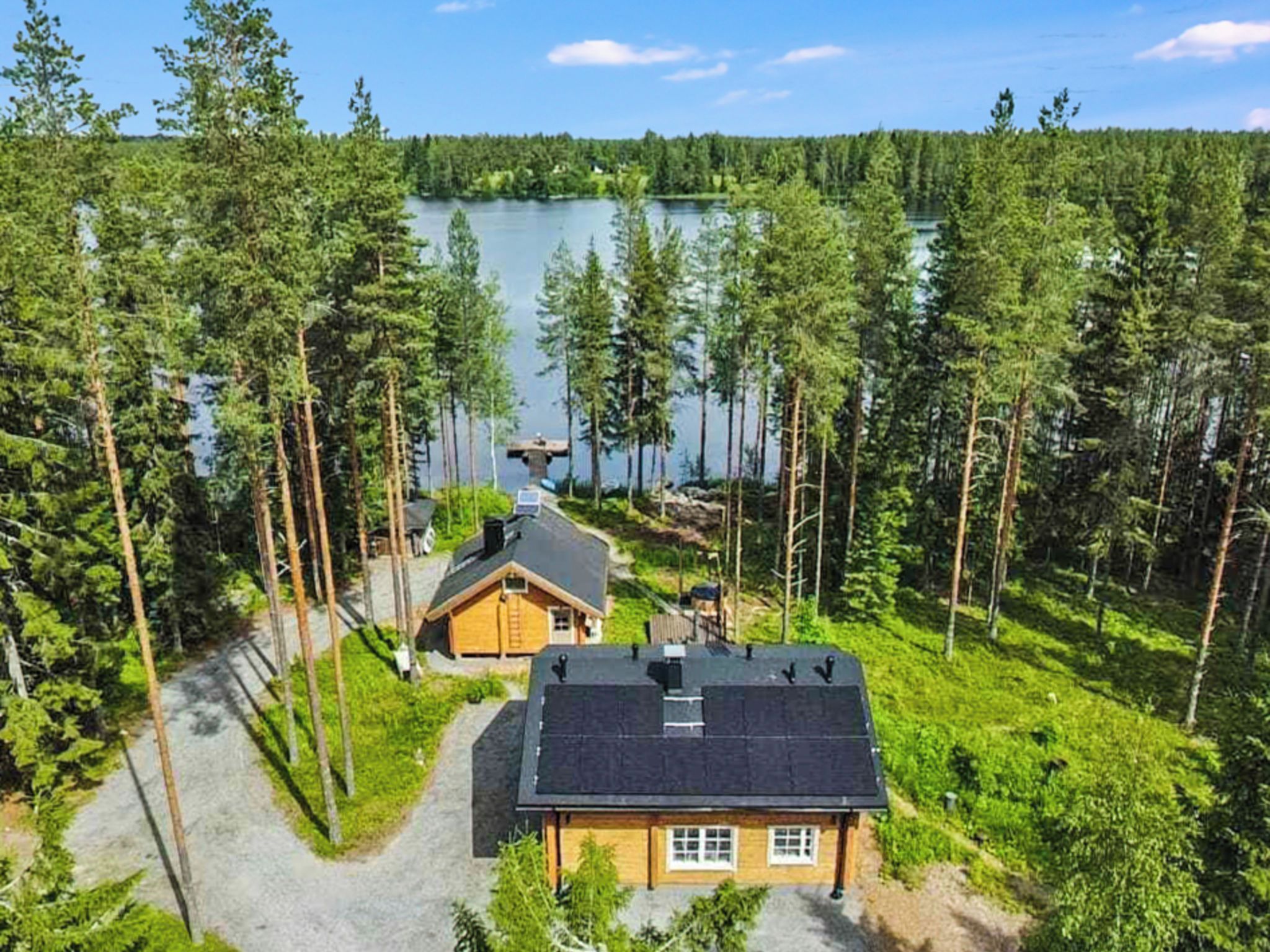 A cabin with a dock extending into a lake, surrounded by dense forest.