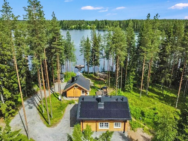 A cabin with a dock extending into a lake, surrounded by dense forest.