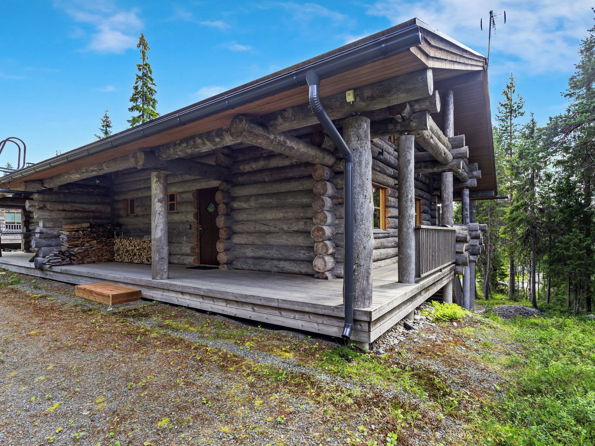 Une cabane en rondins avec une véranda, une cheminée et une pile de bois de chauffage.