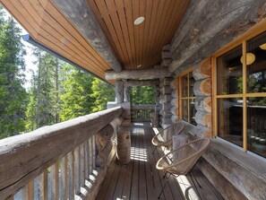 A wooden deck with a railing, two wicker chairs, and a glass window. - Honka 1a by Interhome (Kuusamo)