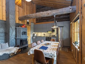 A cozy kitchen with a stone fireplace, wooden beams, and a dining area with a table set for four. - Honka 1a by Interhome (Kuusamo)