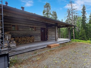 A log cabin with a porch, a stack of firewood, and a gravel driveway. - Honka 1a by Interhome (Kuusamo)