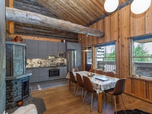 A rustic kitchen with modern appliances, a dining area with wooden chairs, and a stone fireplace. - Honka 1a by Interhome (Kuusamo)