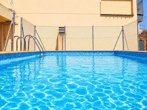 A swimming pool with clear blue water, surrounded by a chain-link fence and metal railings. - Winahost Loft el Rincón de Sants (Barcelona)