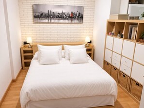 A neatly arranged hotel room with a bed, two bedside tables, a wall-mounted cityscape artwork, and a built-in storage unit with baskets. - Winahost Loft el Rincón de Sants (Barcelona)