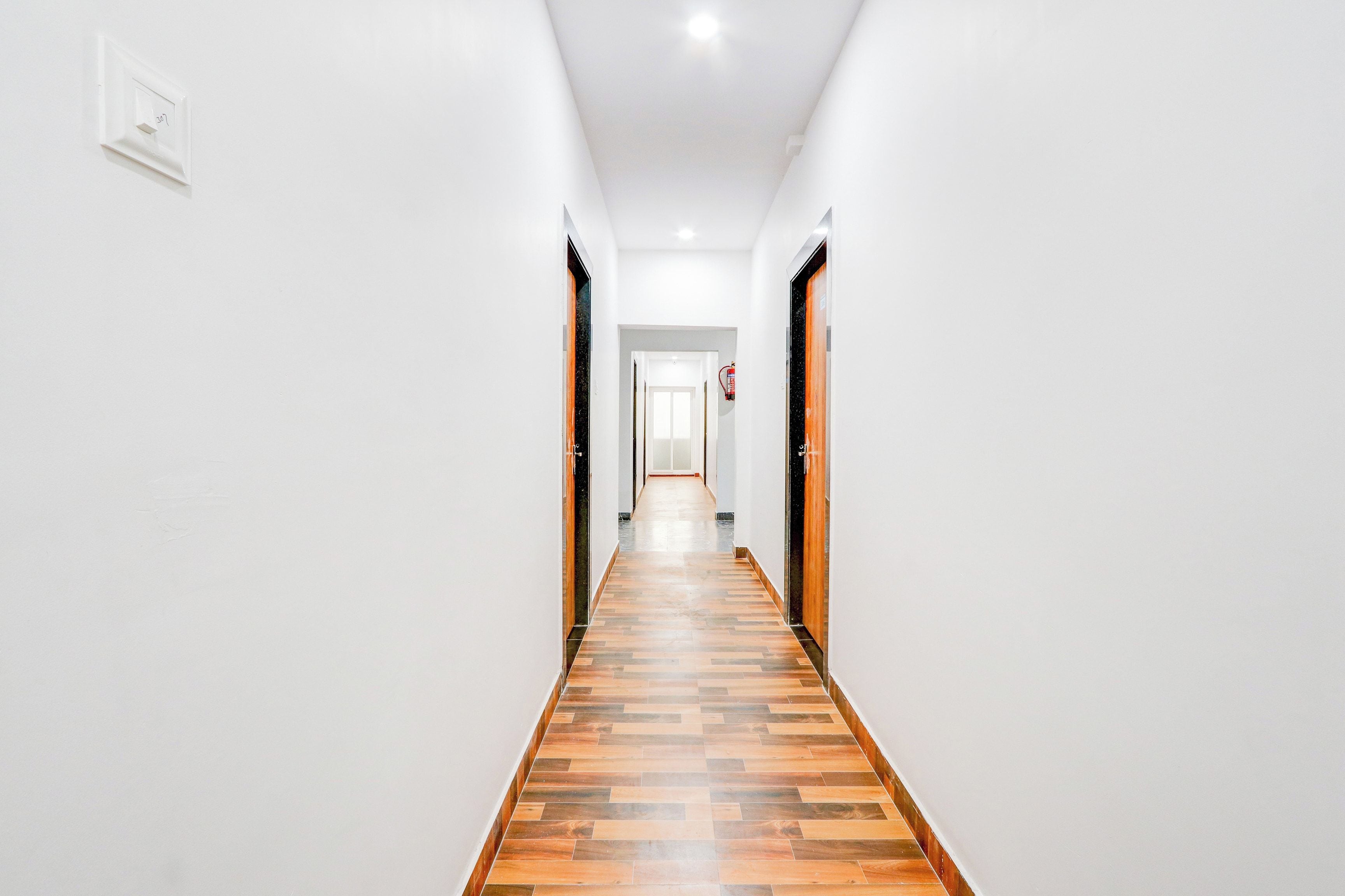 A corridor with a wooden floor, white walls, and doors on both sides.