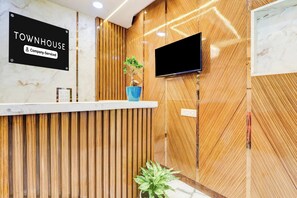 A reception desk with a sign reading 'TOWNHOUSE Company-Serviced,' a flat-screen TV mounted on the wall, and a potted plant on the counter.