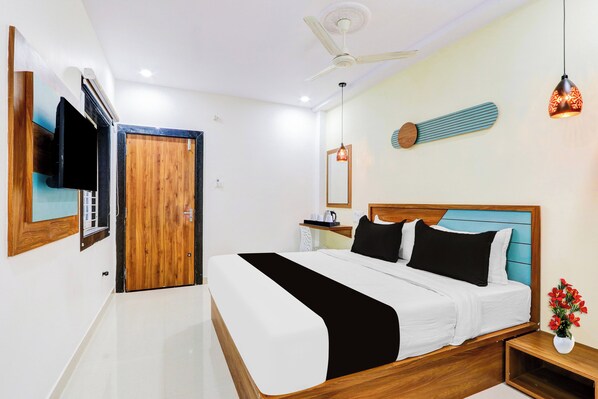 A hotel room with a bed, a television, a ceiling fan, and a nightstand with a vase of flowers.