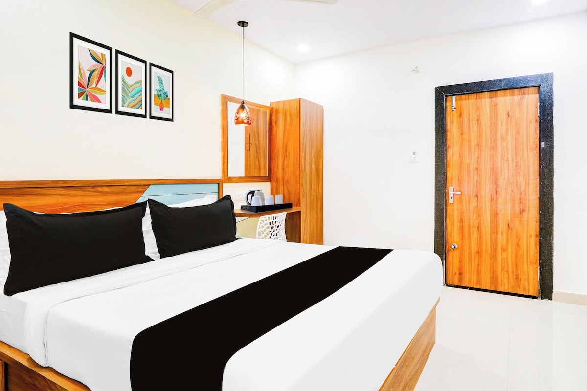 A hotel room with a bed, a wooden wardrobe, a small table with a kettle, and a door.