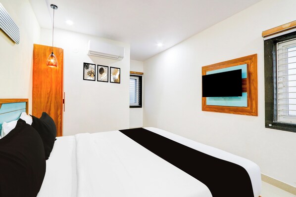 A hotel room with a bed, a wooden door, a window with blinds, and a wall-mounted TV.