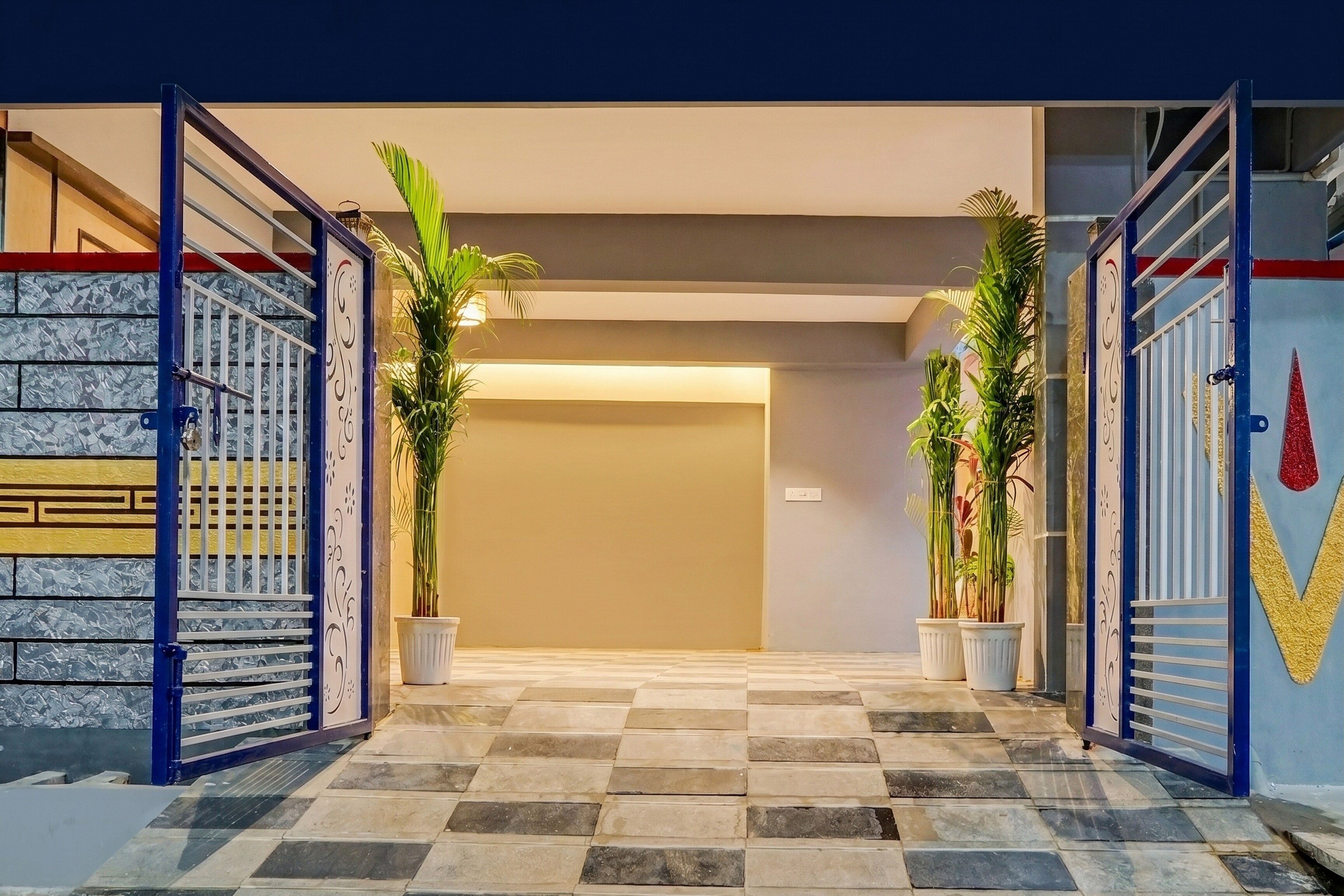Entrada de hotel con piso a cuadros, una puerta metálica y plantas en macetas.