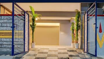 Entrada de hotel con piso a cuadros, una puerta metálica y plantas en macetas.