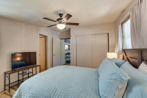 Een slaapkamer met een bed, een televisie, een plafondventilator en een kledingkast.