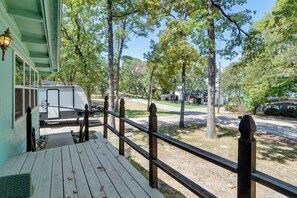 A wooden deck with a railing, a covered area with a bench, and a view of a residential street with houses and trees. - Cedar Creek Lake House! Beautiful Lake Views! (Mabank)