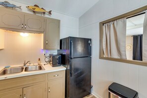 Een kleine keuken met een zwarte koelkast, een spoelbak en houten kastjes.