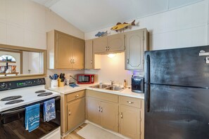 A compact kitchen with a stove, microwave, refrigerator, and wooden cabinets. - Cedar Creek Lake House! Beautiful Lake Views! (Mabank)