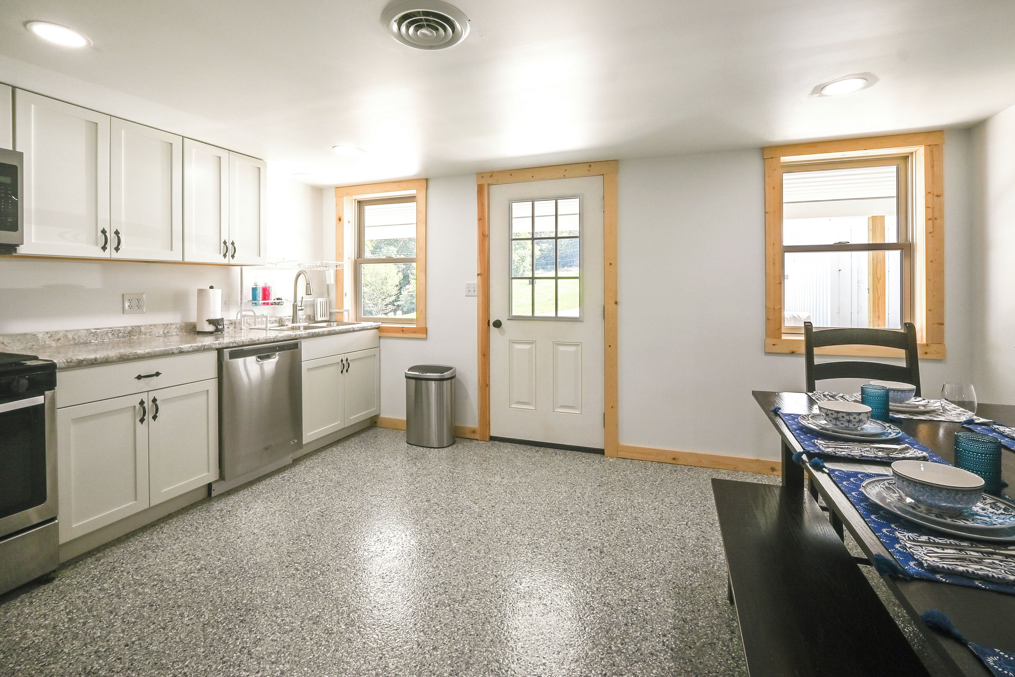 A kitchen with white cabinets, a dishwasher, a trash can, and a dining table set with blue tableware.
