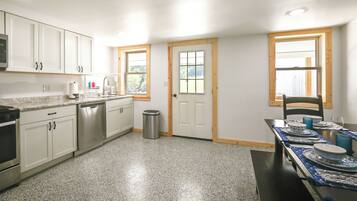 A kitchen with white cabinets, a dishwasher, a trash can, and a dining table set with blue tableware.