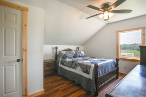 Una camera da letto con soffitto spiovente, un letto con copripiumino decorato, una cassettiera in legno e una finestra che si affaccia sull'esterno.