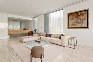 A modern living room with a glass coffee table, a beige sofa, a round ottoman, and a wooden stool. - Muraba Residences - 103-n 2BD (Dubai)