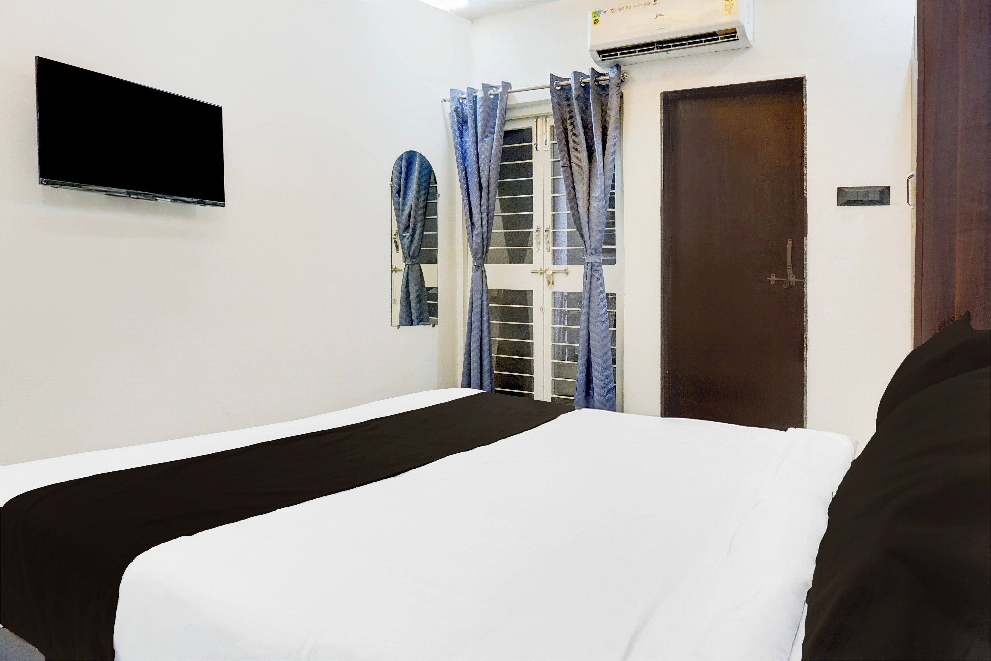 A room with a bed, a television mounted on the wall, and a door with a window.