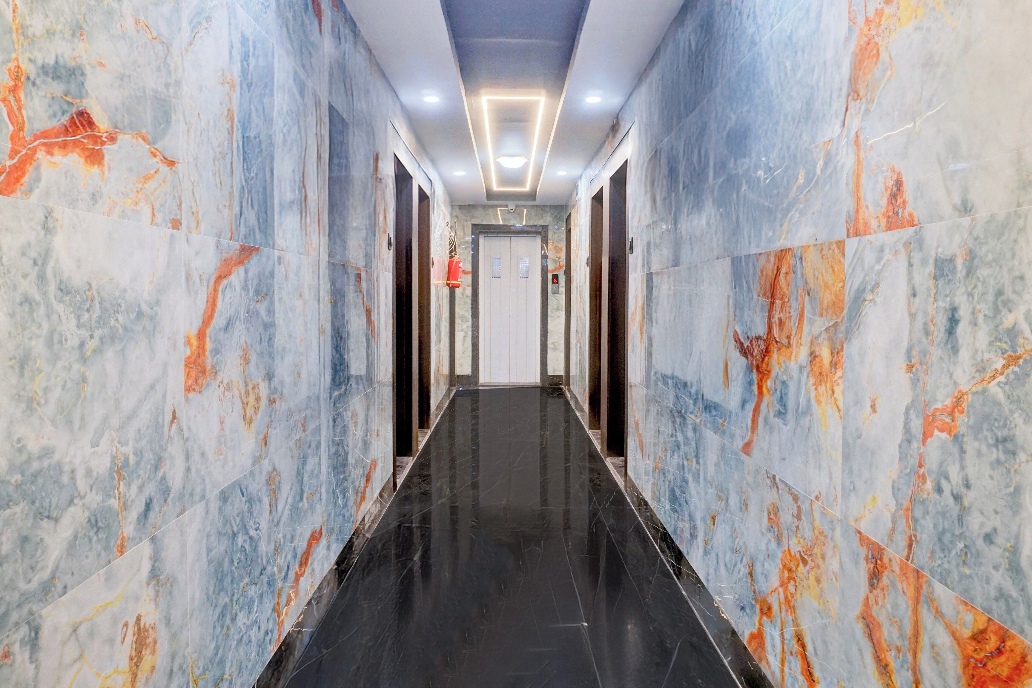 A corridor with marble walls and a black floor, leading to a door with a number sign.