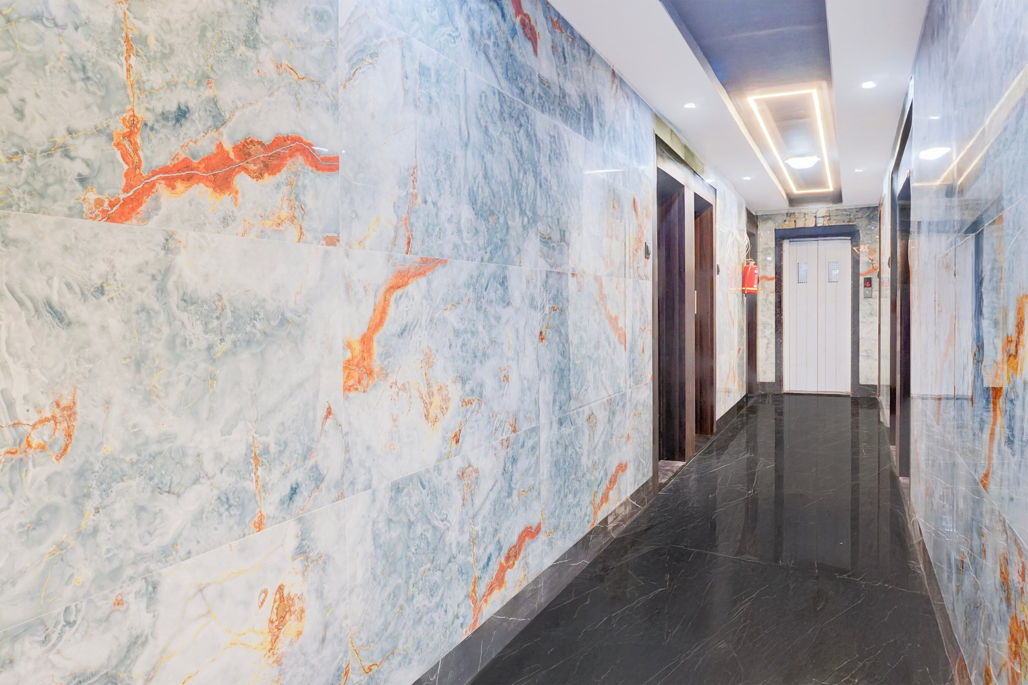 A hallway with marble walls and a black floor, leading to an elevator.
