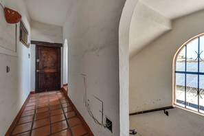 Ein Korridor mit Fliesenboden, einer Holztür und einem Fenster mit Metallgitter.