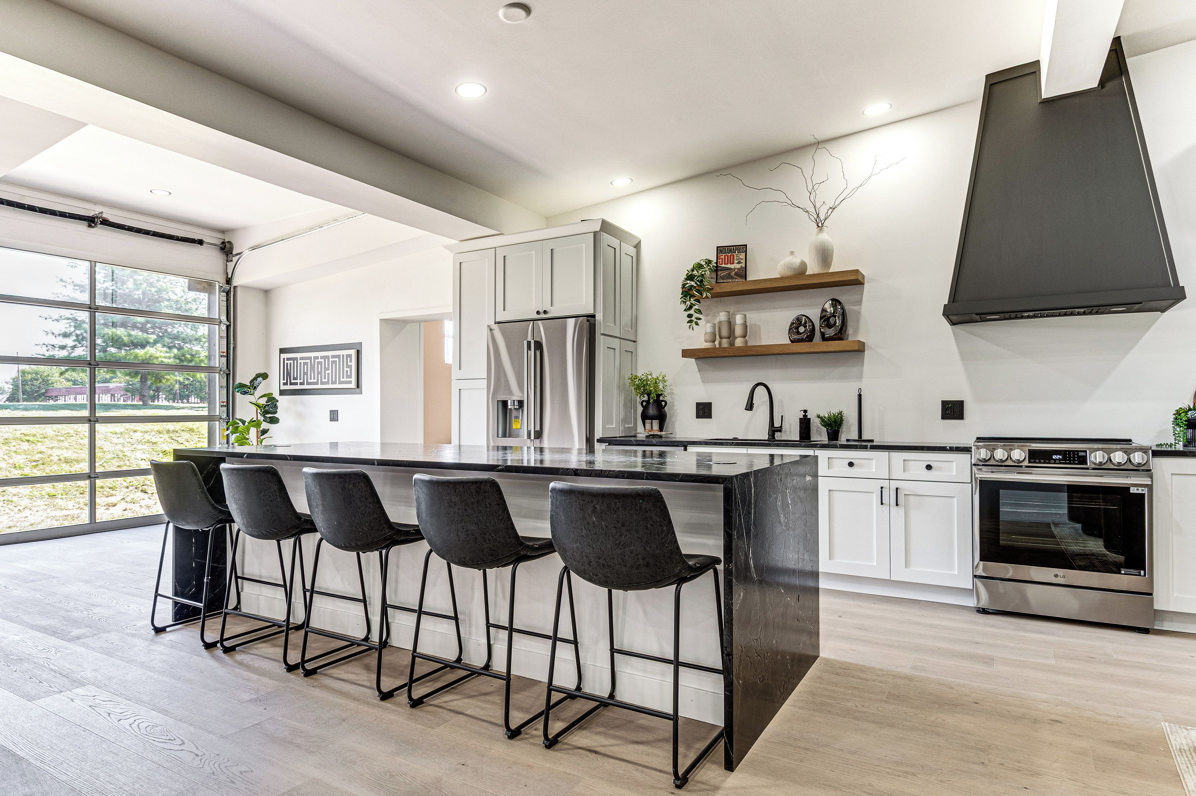 Una cucina moderna con un'isola grande, sgabelli da bar, elettrodomestici in acciaio inossidabile e vista attraverso la porta in vetro.