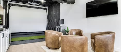 A modern living room with a flat-screen TV, leather sofas, and a projector screen.
