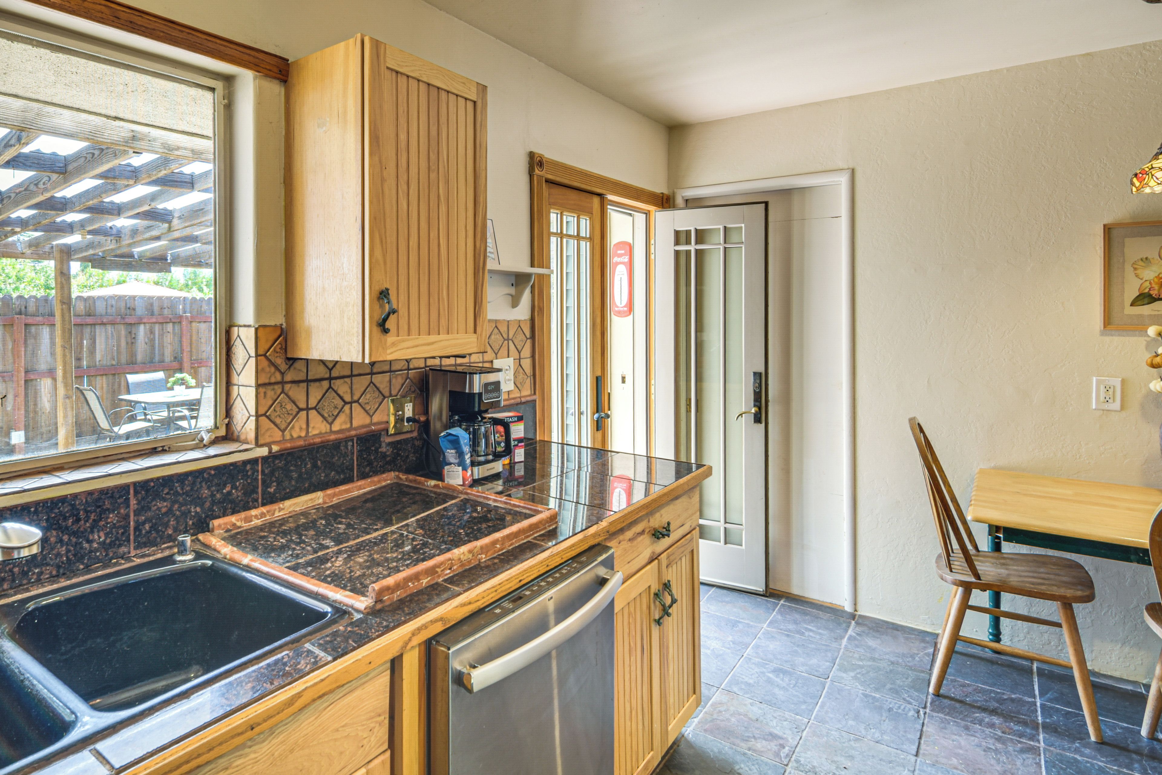 Una cucina con mobili in legno, una lavastoviglie in acciaio inossidabile, un piano di lavoro in granito e un'area pranzo con tavolo e sedie in legno.