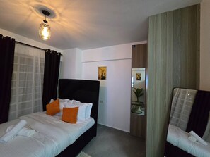 A hotel room with a bed, a chair, a desk, and a ceiling light. - Boma Homes Studio BnB (Nairobi)