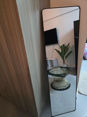 A room with a large mirror reflecting a potted plant, a glass table, and a television on the wall. - Boma Homes Studio BnB (Nairobi)