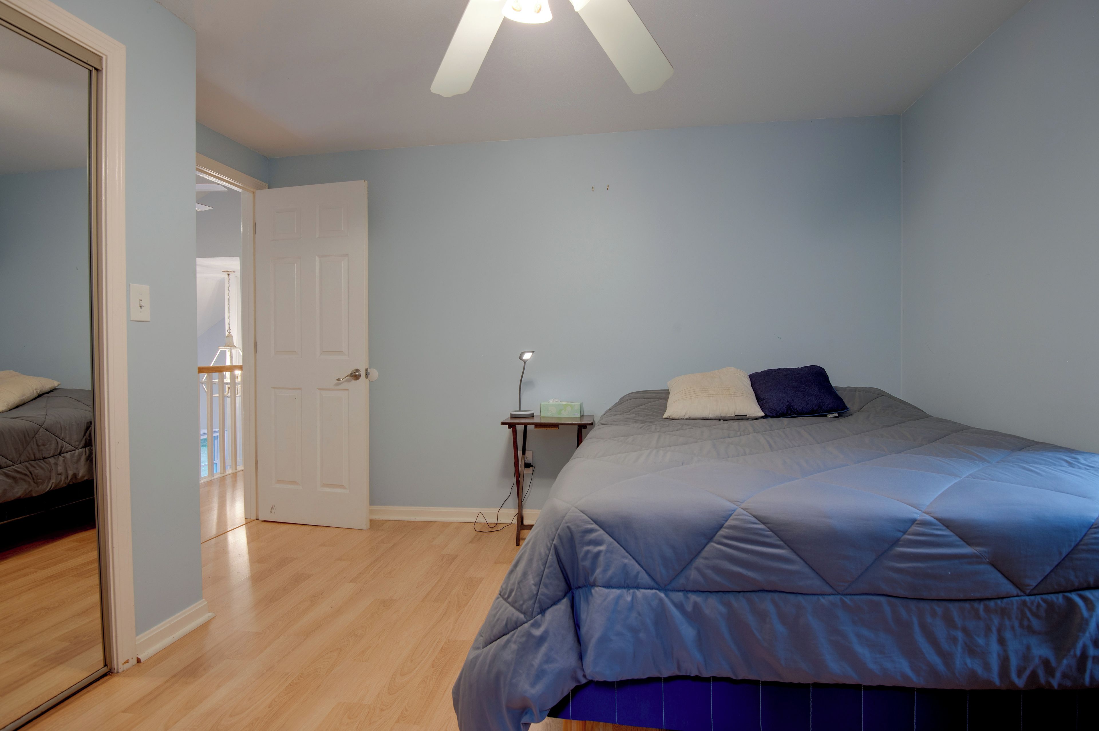 Un dormitorio con una cama, una mesita de noche, una lámpara y una puerta que da a otra habitación.