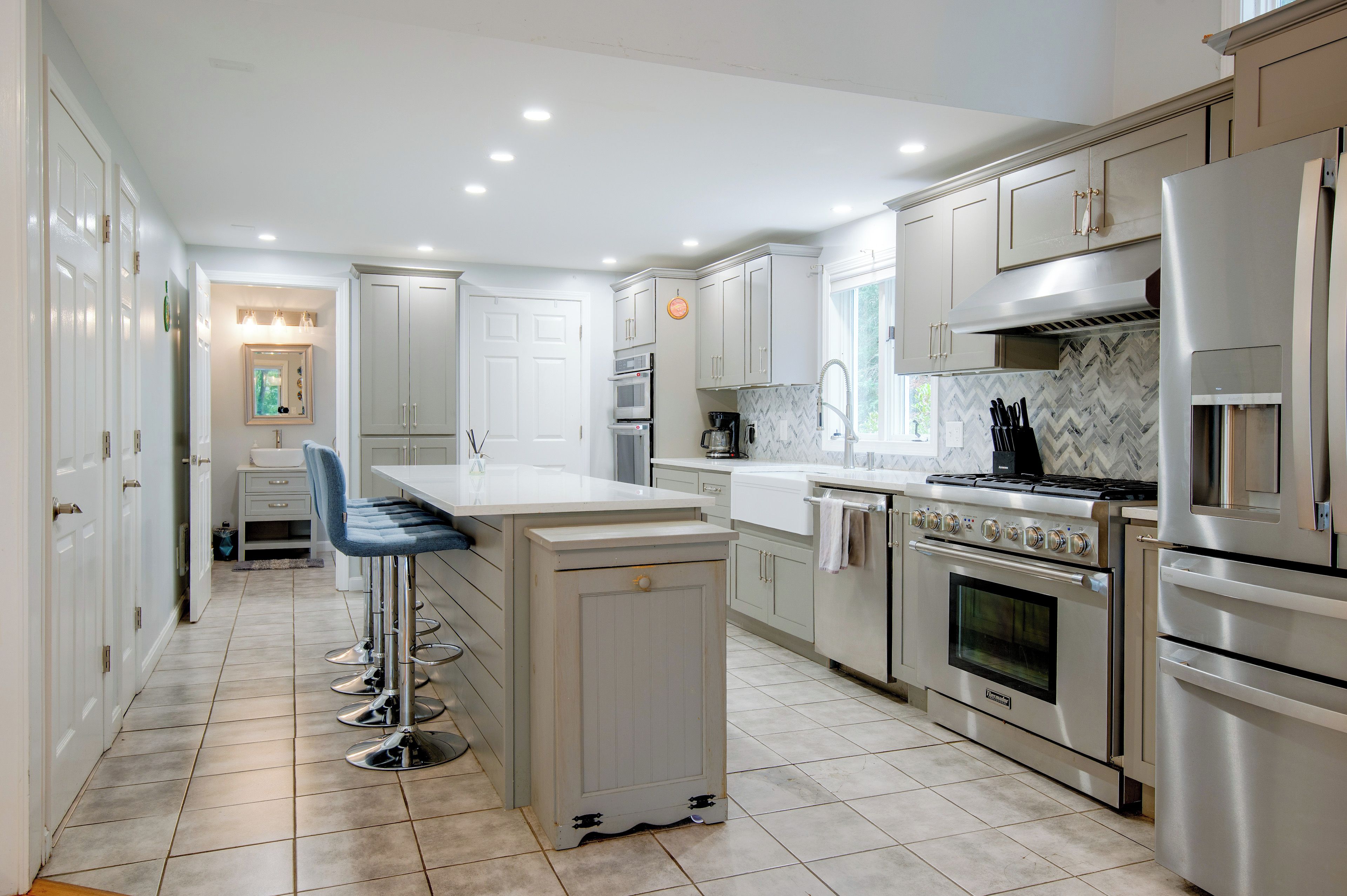 A modern kitchen with a central island, stainless steel appliances, and a herringbone tile backsplash.