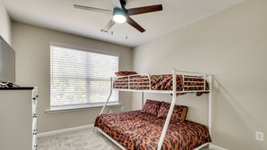 Un lit superposé avec une couvre-lit à motifs léopard, un ventilateur de plafond, une fenêtre avec des stores et un sol recouvert de moquette.