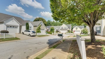 A residential street with houses, a white car parked on the street, and a mailbox.
