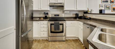 A modern kitchen with white cabinetry, stainless steel appliances, and a granite countertop.