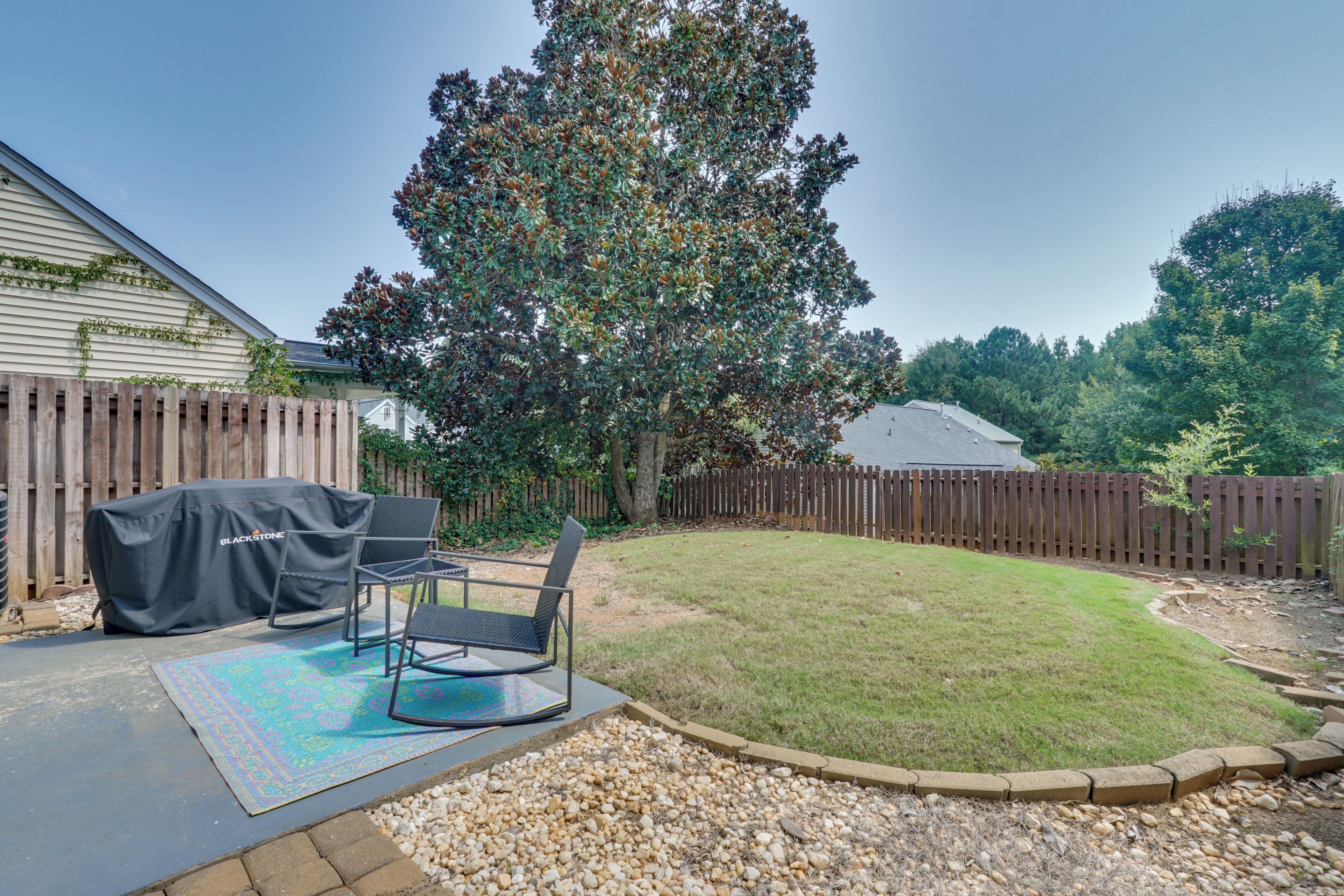 A backyard with a patio, outdoor furniture, a covered grill, and a large tree.