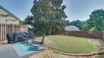 A backyard with a patio, outdoor furniture, a covered grill, and a large tree.