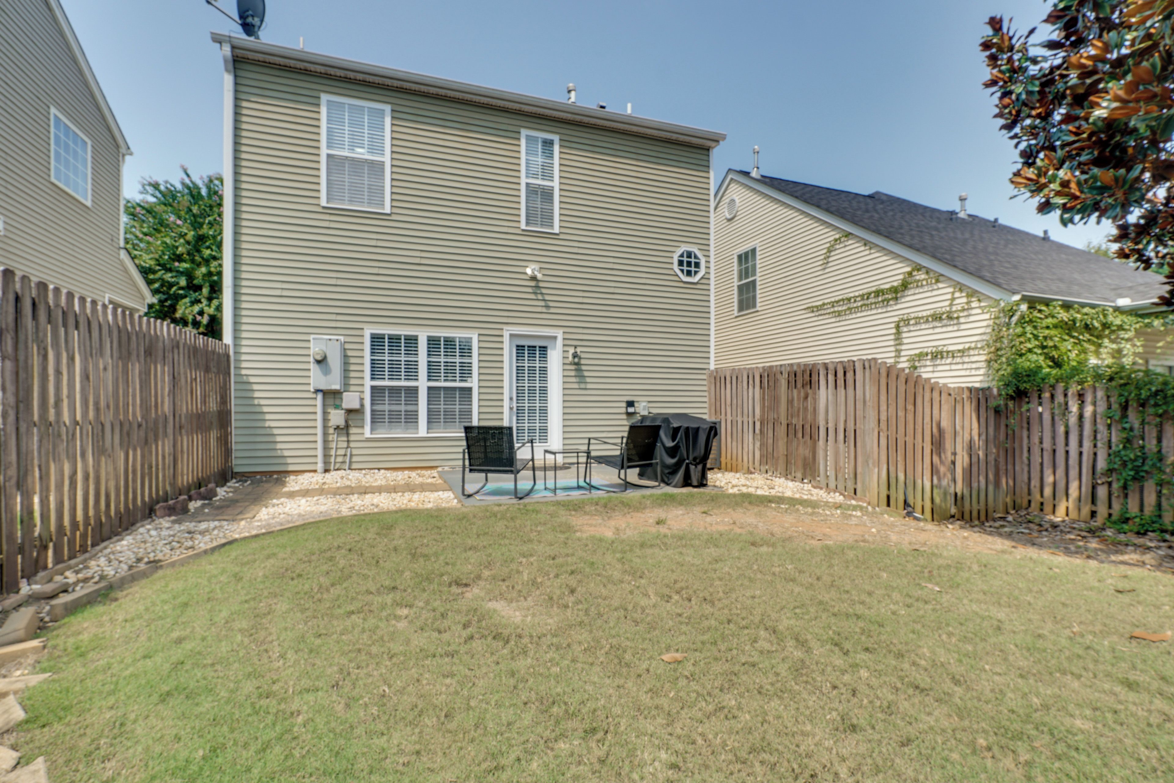 A residential backyard with a lawn, a barbecue grill, and a covered patio area.