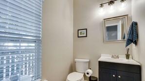 Une salle de bain avec des toilettes, un lavabo et une fenêtre équipée de stores.