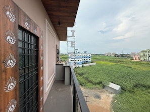 A balcony with a view of a blue building and green fields. - HOTEL SHREESH MAYAPUR (Krishnanagar)