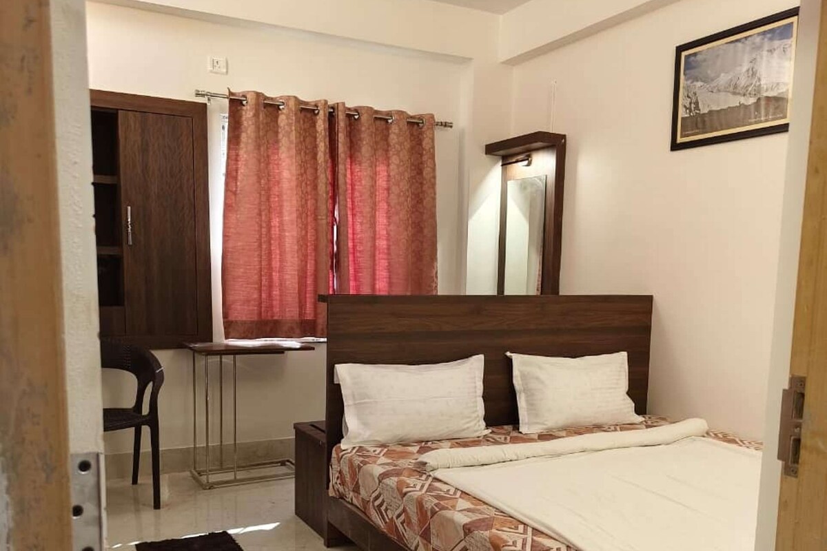 Un dormitorio con cama, escritorio, silla, espejo y ventana con cortinas.